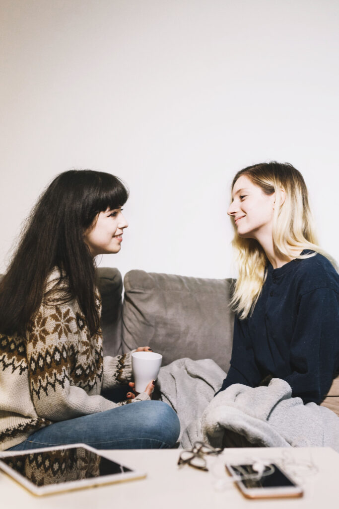 Two girls sitting on couch talking to each other